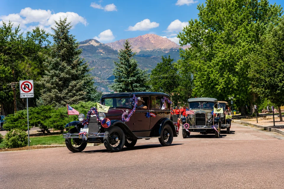 Classic cars driving with Pikes Peak in the background during a Colorado Springs event.