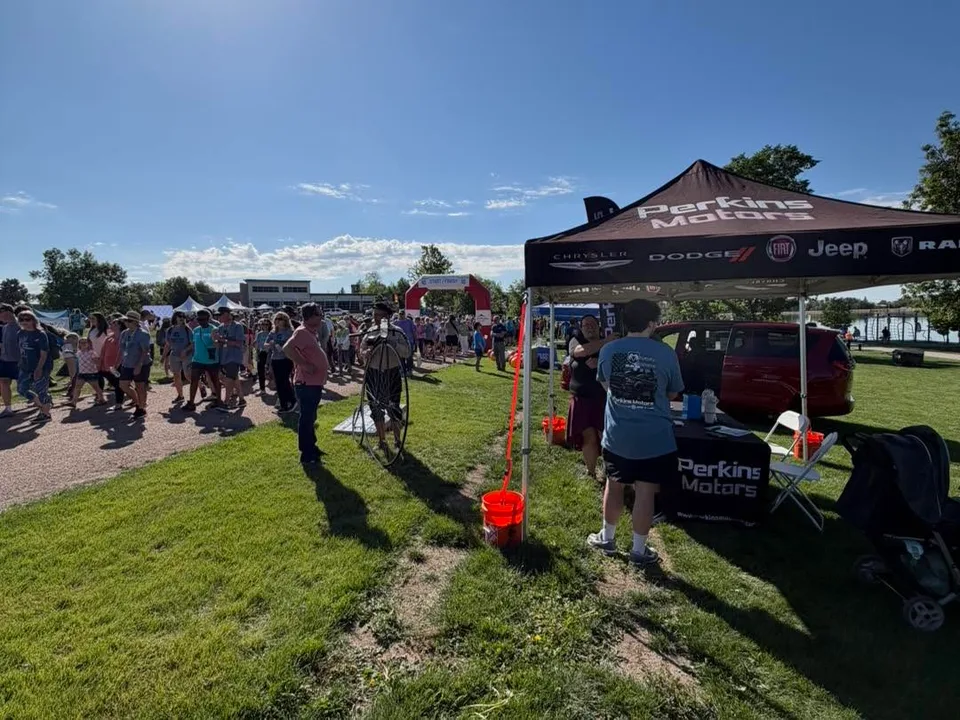 Outdoor event crowd gathered near a Perkins Motors tent on a sunny day.